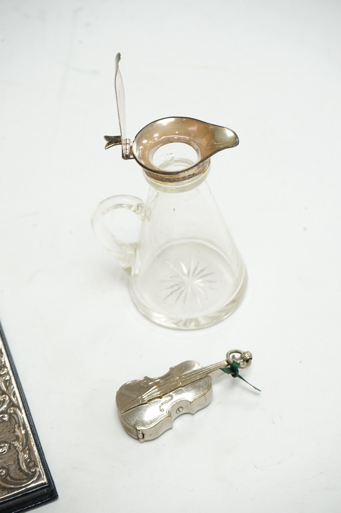 A George V silver mounted glass whisky noggin, by Levi & Salaman, Birmingham, 1911, 10.2cm, together with a modern repousse silver mounted address book, by Keyford Frames Ltd, London, 1989 and a plated novelty violin ves